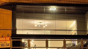 A building with a tiled facade, a visible window with reflections, and a sign with contact information.
