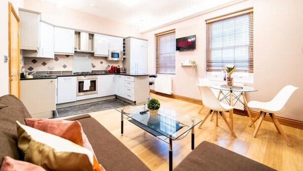 A compact living space with a kitchenette, a dining area with a glass table, and a TV mounted on the wall. - St Paul Cathedral-City of London]London Apartment (London)