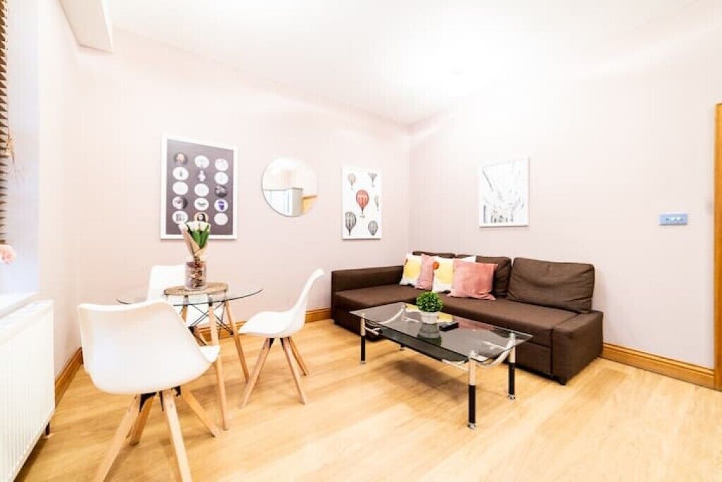 A modern living room with a brown sofa, white chairs, a glass coffee table, and artwork on the walls.