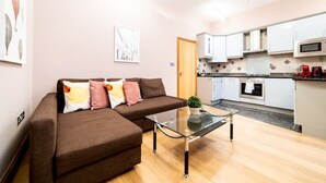 A modern living room with a brown sofa, a glass coffee table, and a kitchen area with white cabinets and a microwave. - St Paul Cathedral-City of London]London Apartment (London)