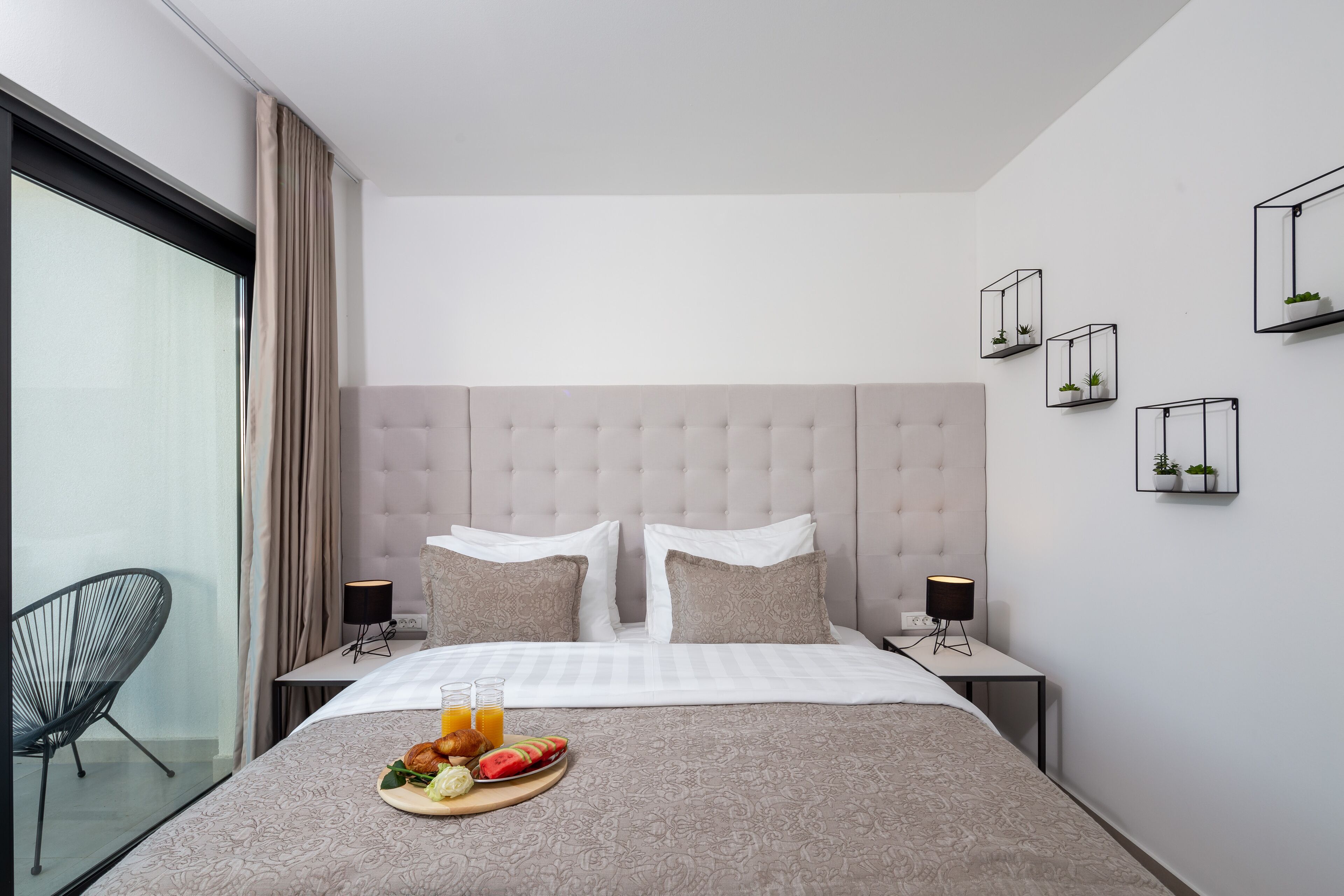 A modern hotel room with a large bed, two bedside tables, a chair, and a glass wall.