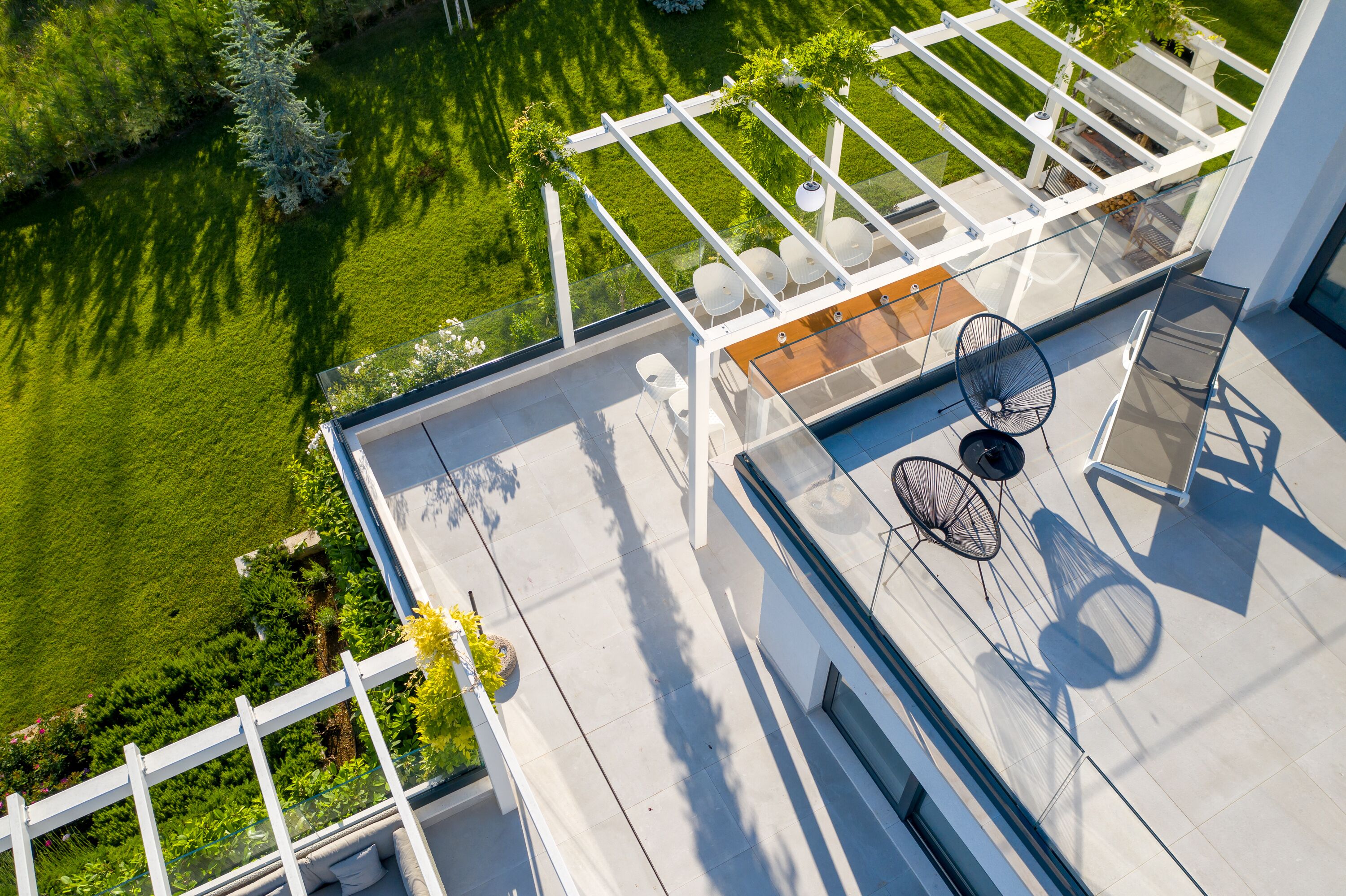 Vue aérienne d’une terrasse sur le toit, dotée d’une balustrade en verre, d’un espace salon extérieur et offrant une vue sur une pelouse bien entretenue.