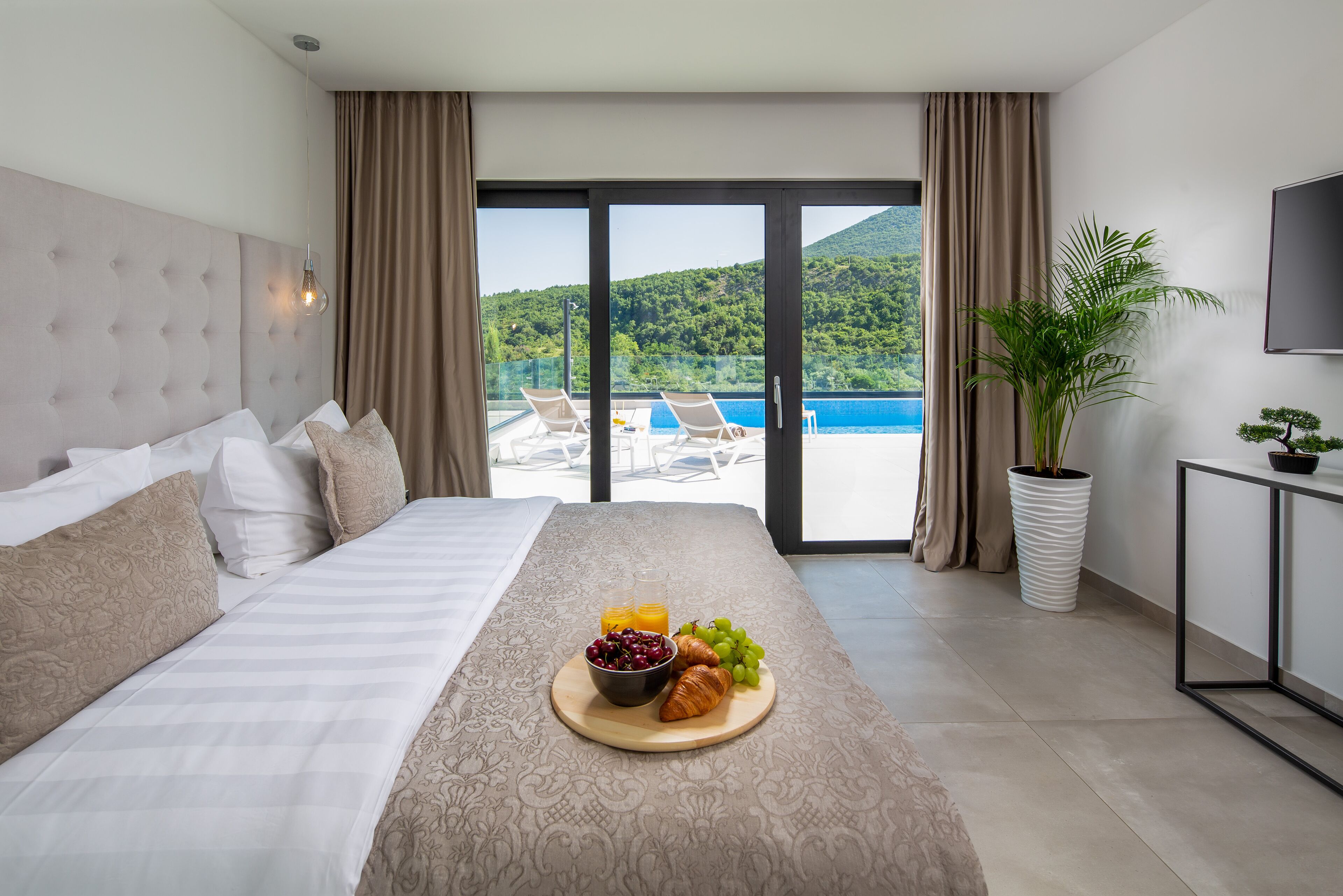 A hotel room with a bed, breakfast tray, and a view of a pool and mountains.