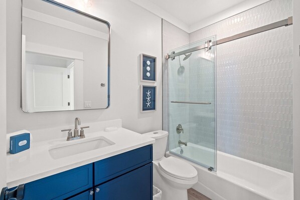 A modern bathroom with a white sink, blue cabinets, a toilet, and a glass-enclosed shower.