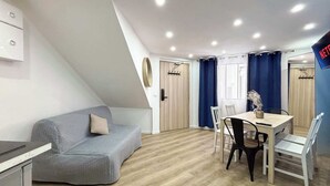 Una habitación moderna y luminosa con un sofá gris, una mesa de comedor de madera con sillas y una zona de cocina con armarios.