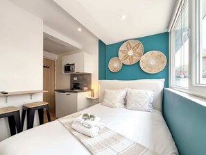Moderni hotellihuone, jossa on sänky, pieni keittonurkkaus ja näkymä ulos.