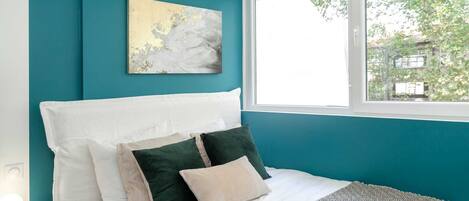 Um quarto com uma cama, uma janela e um quadro na parede.