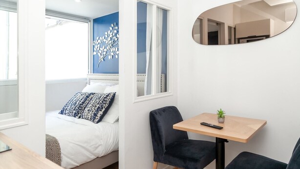 A modern bedroom with a bed, a bedside table, a chair, a small table, and a mirror. - David D Angers 25 - One Bedroom Apartment, Sleeps 2 (Paris)