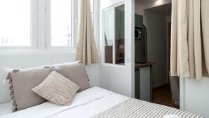 A bedroom with a bed, pillows, a window, and a view of a kitchen area. - David D Angers 26 - One Bedroom Apartment, Sleeps 2 (Paris)