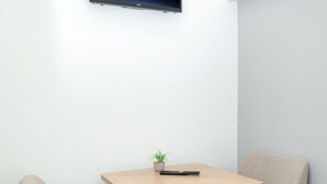 A corner room with a wooden table, two beige chairs, a small potted plant, and a mounted TV on the wall. - David D Angers 26 - One Bedroom Apartment, Sleeps 2 (Paris)