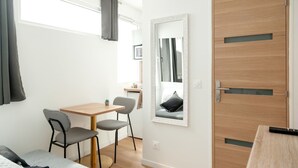 Una habitación pequeña y moderna con puerta de madera, un espejo, una mesa con dos sillas y una cama.