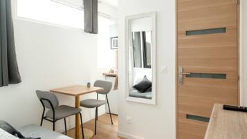 Une petite pièce moderne avec une porte en bois, un miroir, une table avec deux chaises et un lit.