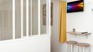 Een moderne woonkamer met een bank, een klein houten tafeltje, een aan de muur bevestigde televisie en een geel gordijn.