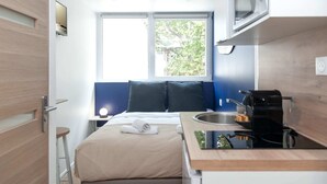 A compact hotel room with a bed, a small bedside table, a window with a view of trees, a microwave, and a sink with a kettle. - David D Angers 22 - Studio Apartment, Sleeps 2 (Paris)