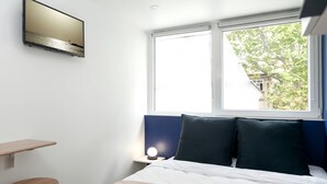 A hotel room with a bed, a desk, a chair, a TV mounted on the wall, and a window with a view of trees. - David D Angers 22 - Studio Apartment, Sleeps 2 (Paris)