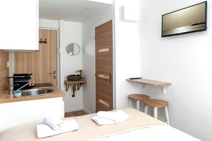 A modern hotel room with a wooden door, a round mirror, a sink, a small table, two stools, and a TV mounted on the wall. - David D Angers 22 - Studio Apartment, Sleeps 2 (Paris)