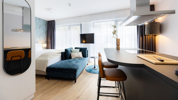 A modern hotel room with a sofa, a dining area, a TV, and a large mirror. - The Doorman Goethe  (Frankfurt)