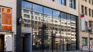 A modern building facade with large glass windows reflecting nearby buildings. - The Doorman Goethe  (Frankfurt)