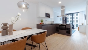 A modern kitchen with white cabinetry, a central island, and a dining area with a white table and brown chairs. - The Doorman Goethe  (Frankfurt)