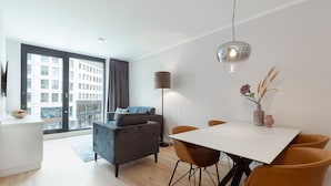 A modern living room with a sofa, a dining table with chairs, a floor lamp, and a view of a cityscape through large windows. - The Doorman Goethe  (Frankfurt)