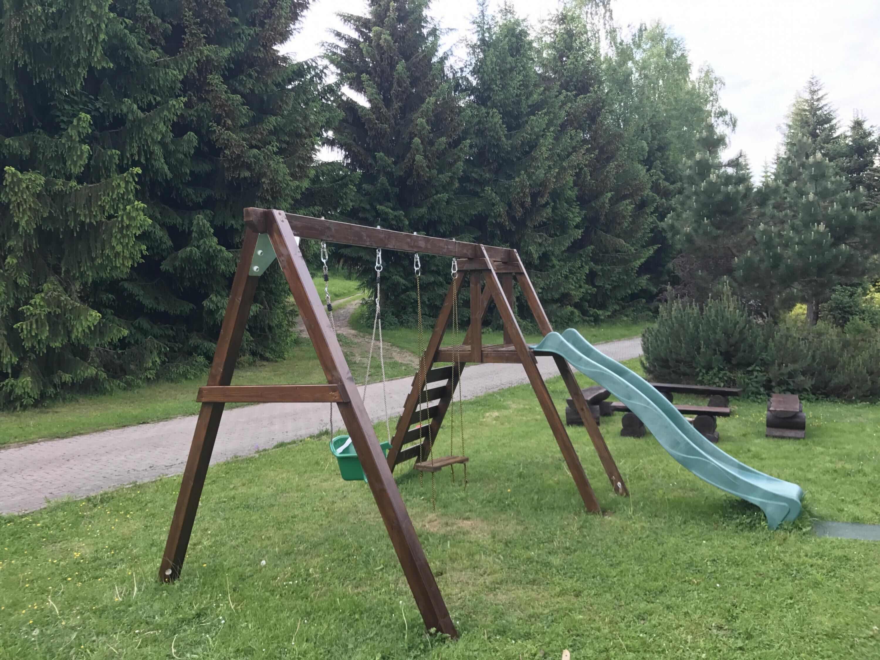 A wooden swing set with a slide in a park.