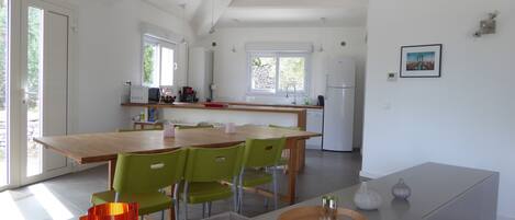 A modern kitchen with a wooden dining table, green chairs, and a white refrigerator.