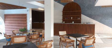 Un intérieur moderne comprenant un coin repas avec des chaises en bois et une table noire, une cuisine avec des meubles en bois et un sol en béton.