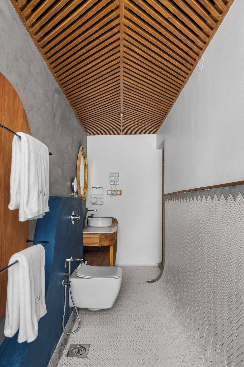 Een moderne badkamer met een houten spilplafond, een blauwe wastafelmeubel, een witte wastafel en een wit toilet.