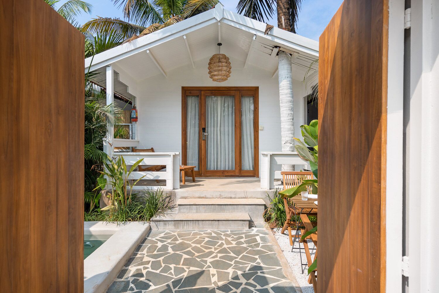 A white building with a wooden door, a covered porch, and a stone-tiled entrance.