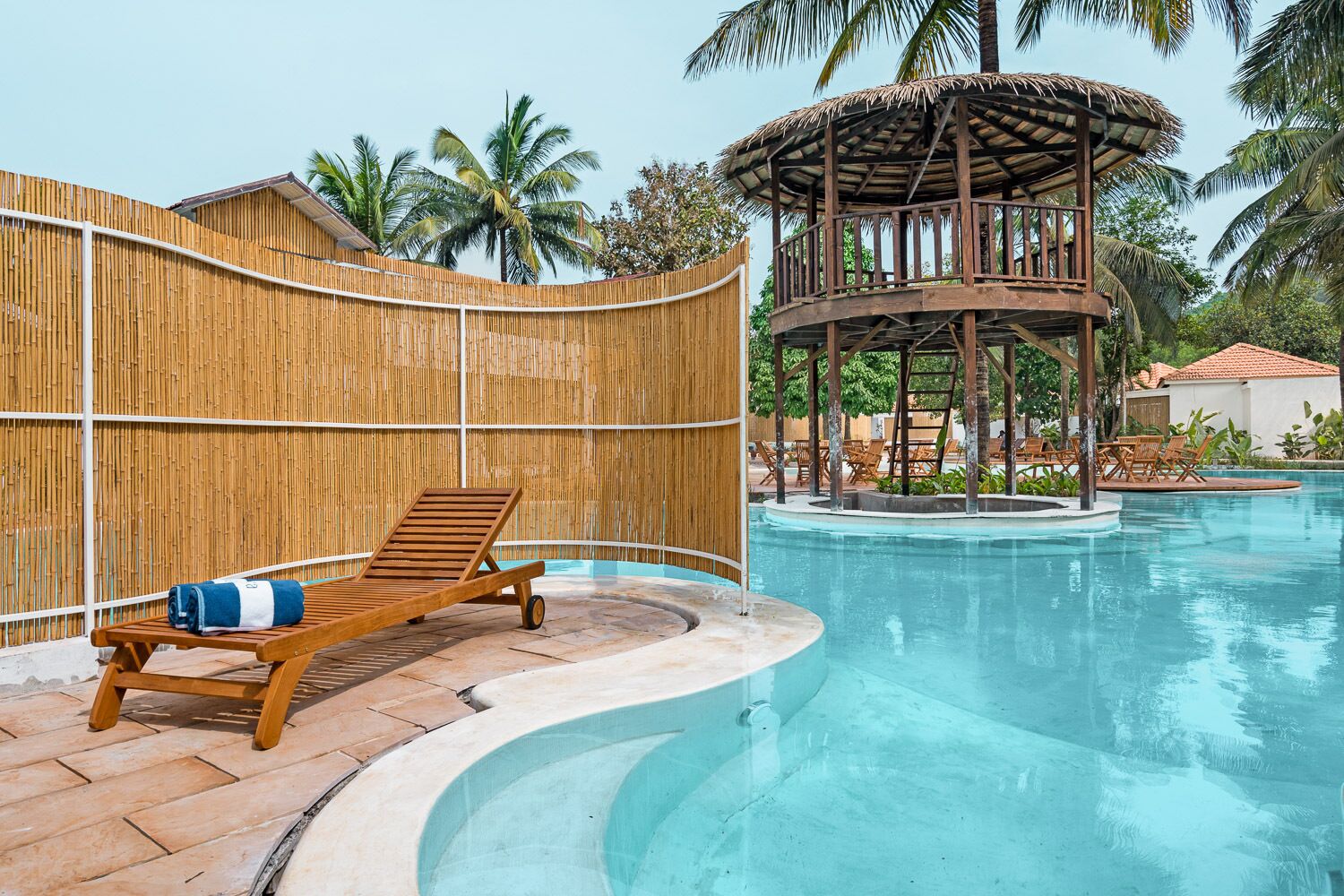 A pool area with a wooden lounge chair, a bamboo fence, and a gazebo structure.