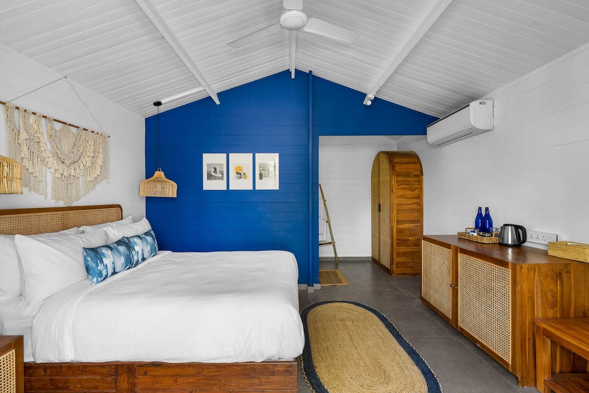 A bedroom with a bed, a blue accent wall, a wooden wardrobe, and a ceiling fan.