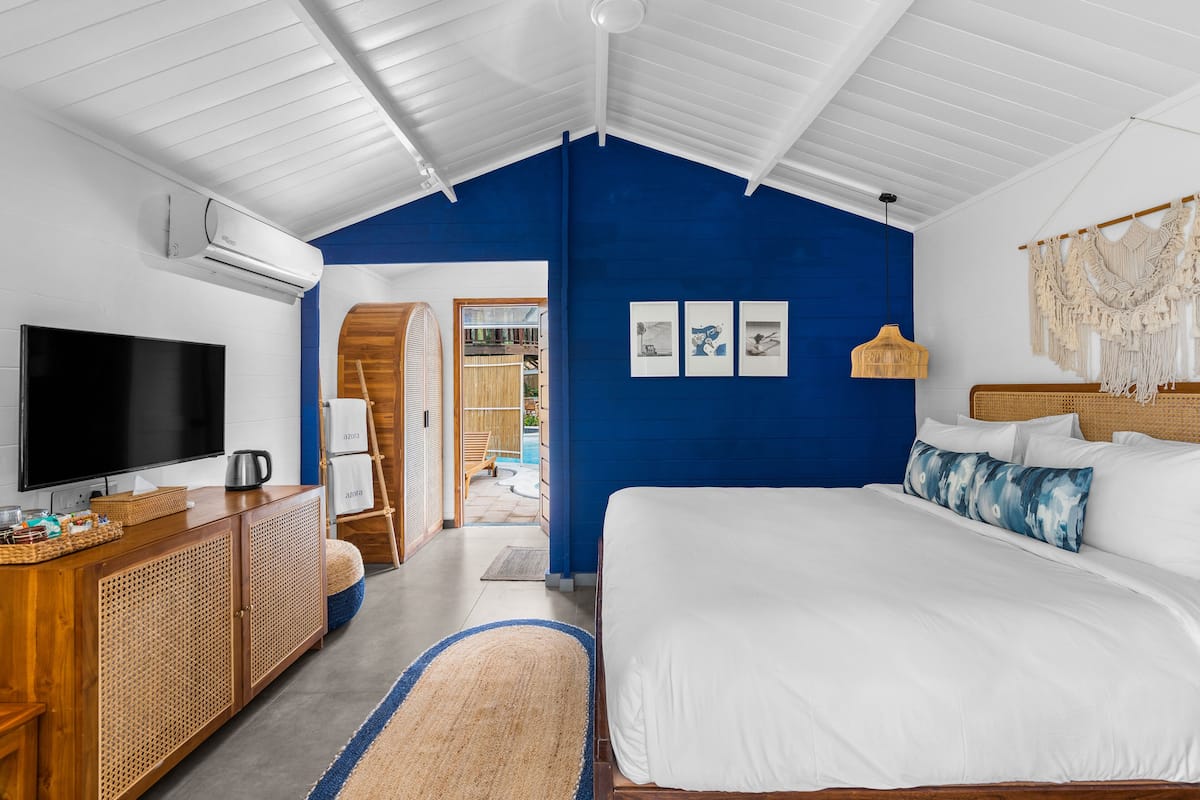A bedroom with a large bed, a TV, a wooden dresser, and a blue accent wall.