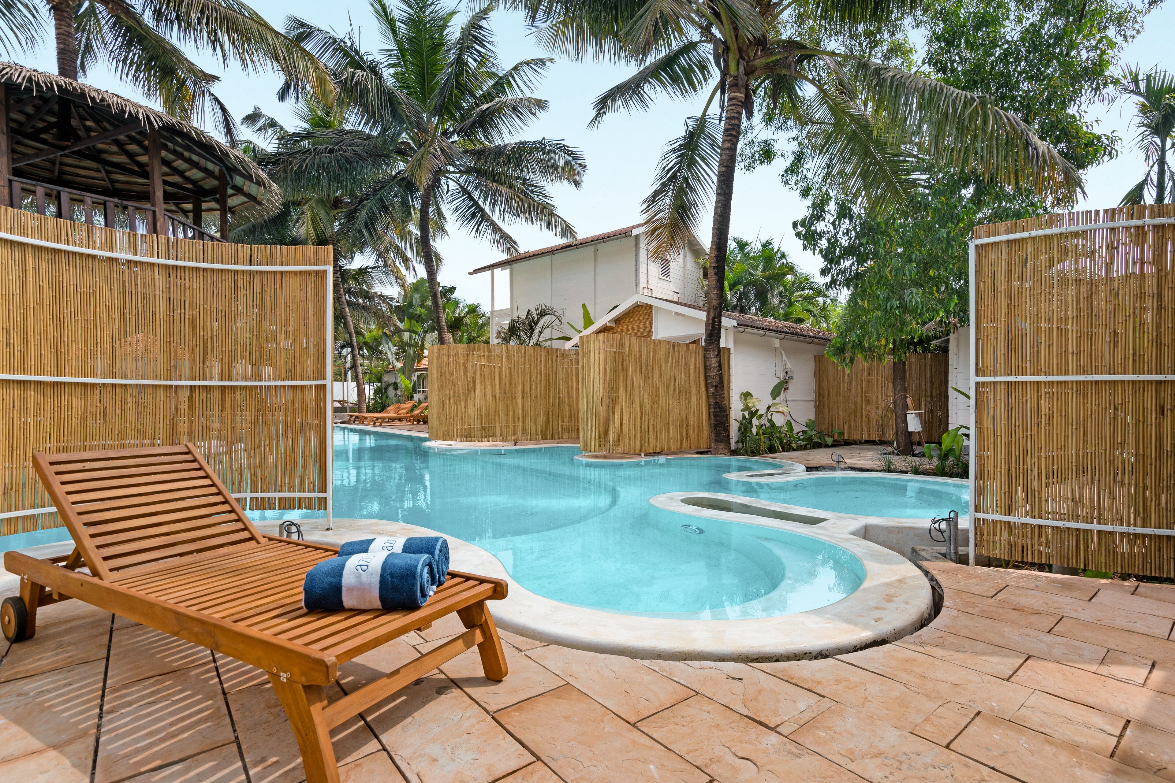 Uma área de piscina com espreguiçadeira de madeira, ofurô e cercas de bambu.