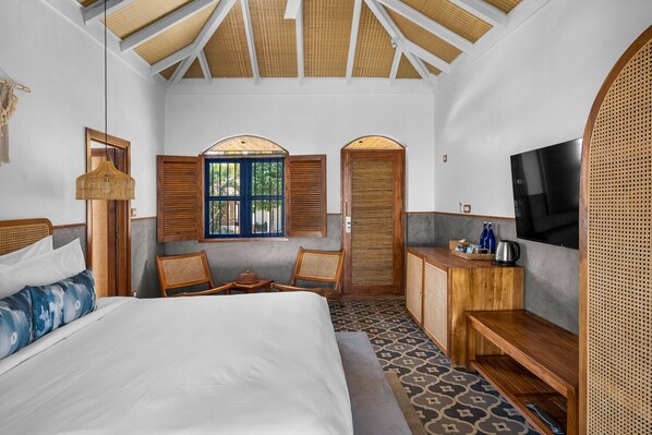Una habitación de hotel con una cama, dos sillas, una mesita, un televisor y una ventana con contraventanas.