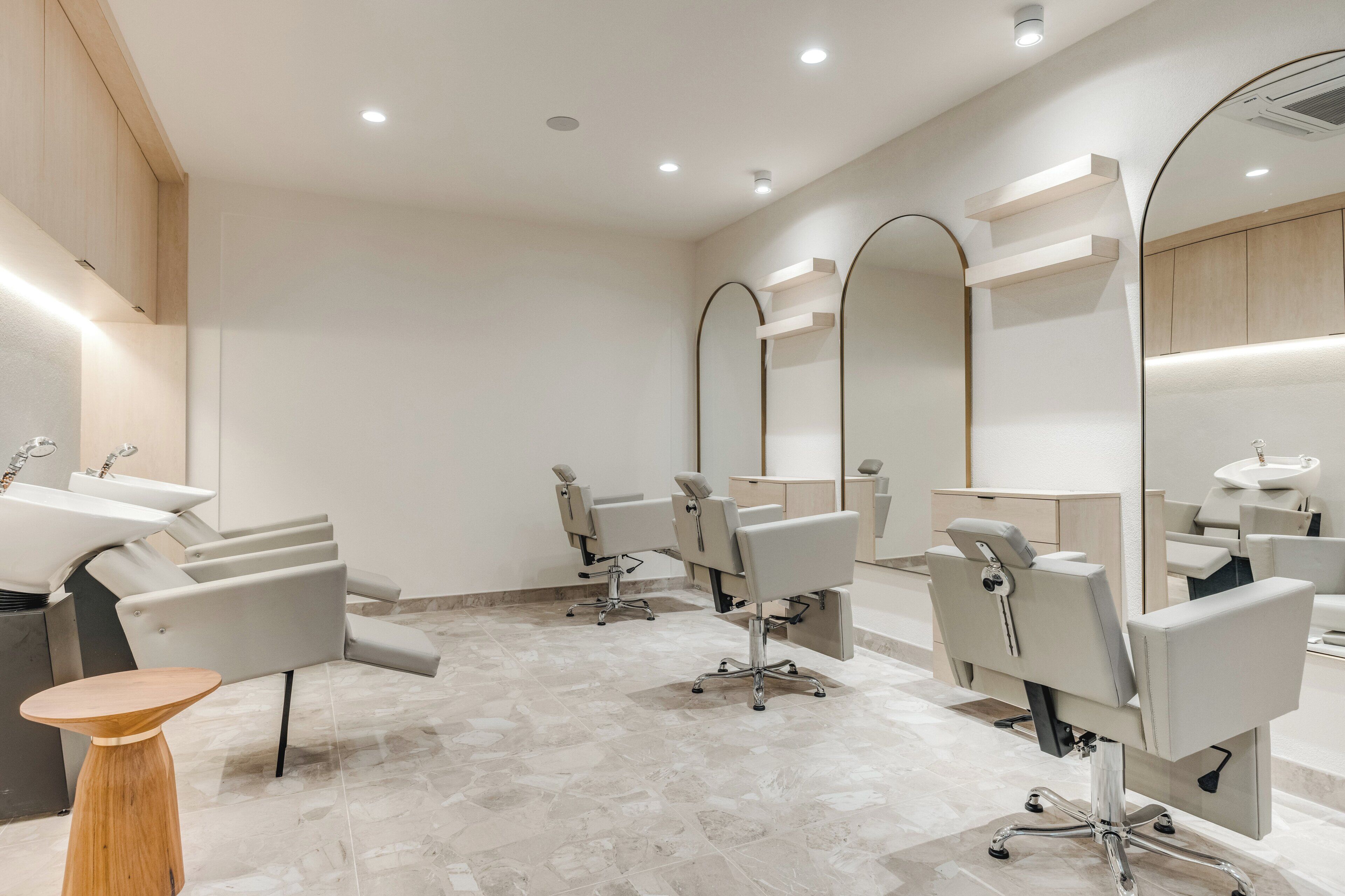 A modern salon with multiple hairdressing stations, each with a chair and a mirror.
