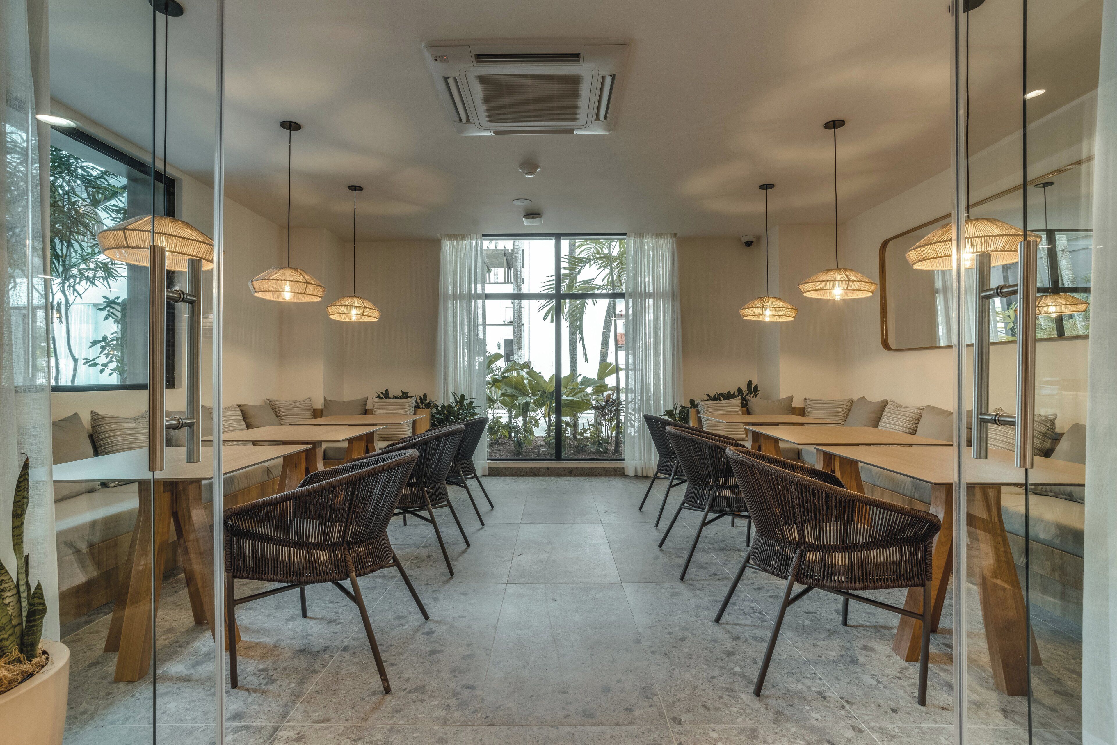 A modern dining area with glass partitions, wicker chairs, and pendant lighting.