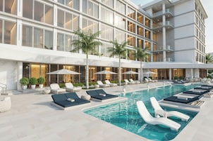 Un hotel moderno con zona de piscina, sillones de descanso y palmeras.