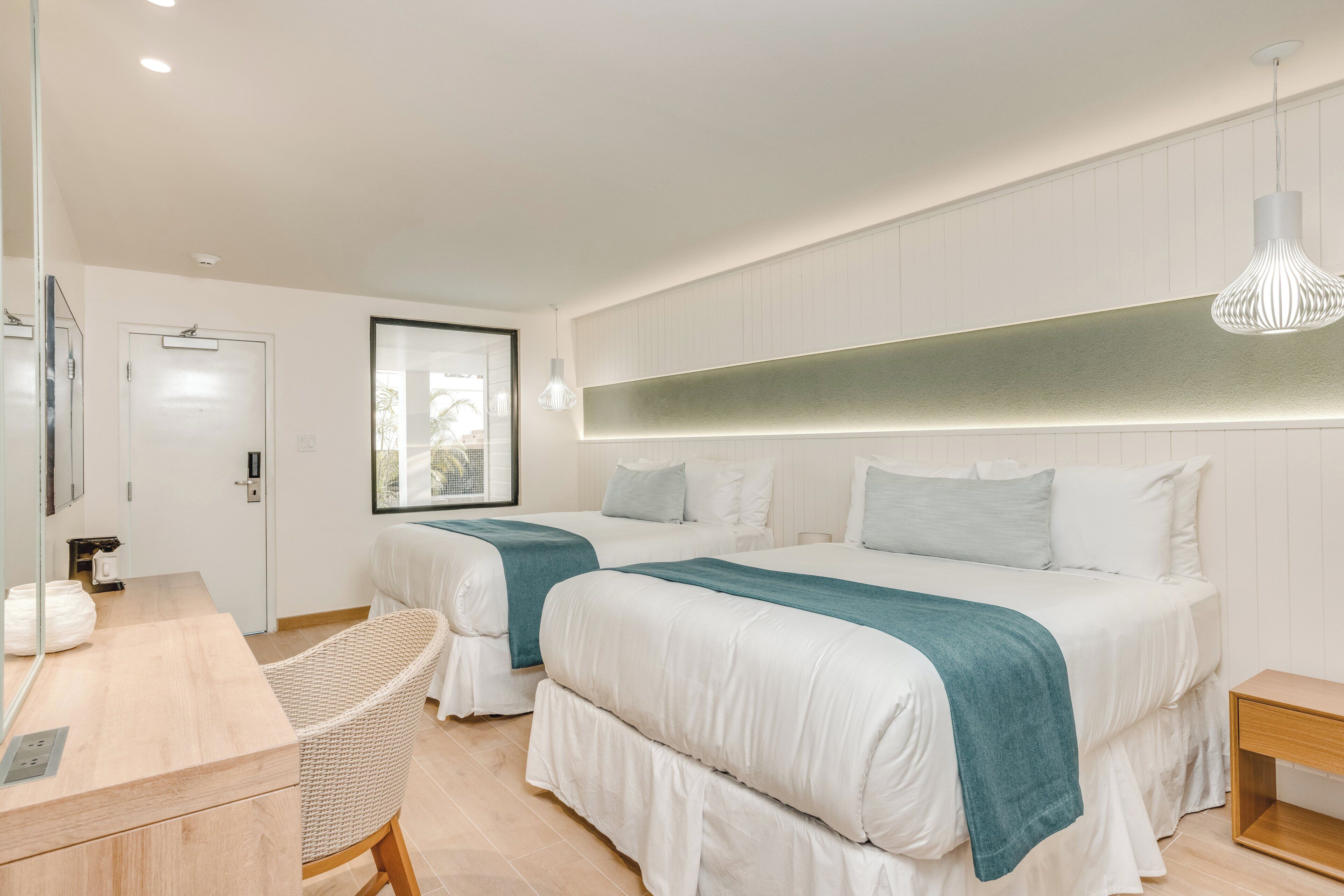A modern hotel room with two beds, a desk, a chair, and a large window.