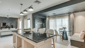 A modern kitchen with a central island, dining area with chairs, and a seating area with a sofa and table.