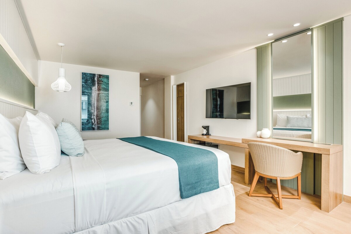 A modern bedroom with a large bed, a desk, a chair, and a television.