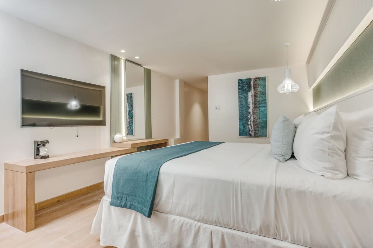 A modern bedroom with a bed, bedside table, mirror, artwork, and pendant light.