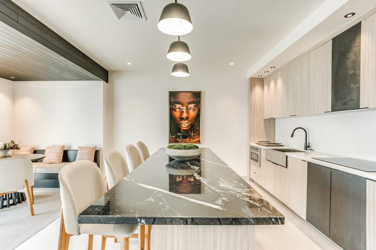 A modern kitchen with a marble countertop, pendant lighting, and a large artwork above the sink.
