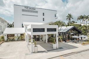 Un hotel moderno con fachada blanca, un área de estar techada al aire libre y palmeras al fondo.