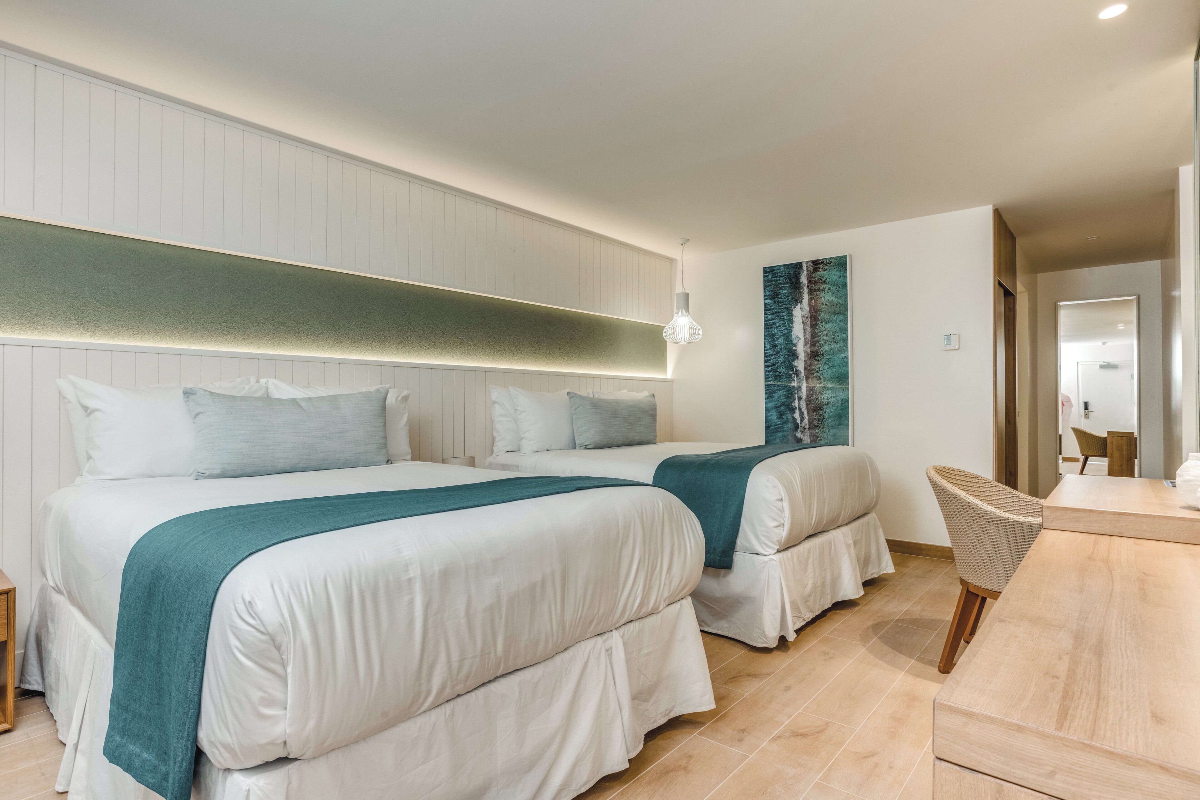A hotel room with two beds, a desk, and a chair.