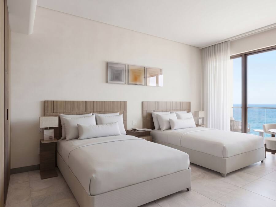 A hotel room with two beds, a small table, and a view of the sea.