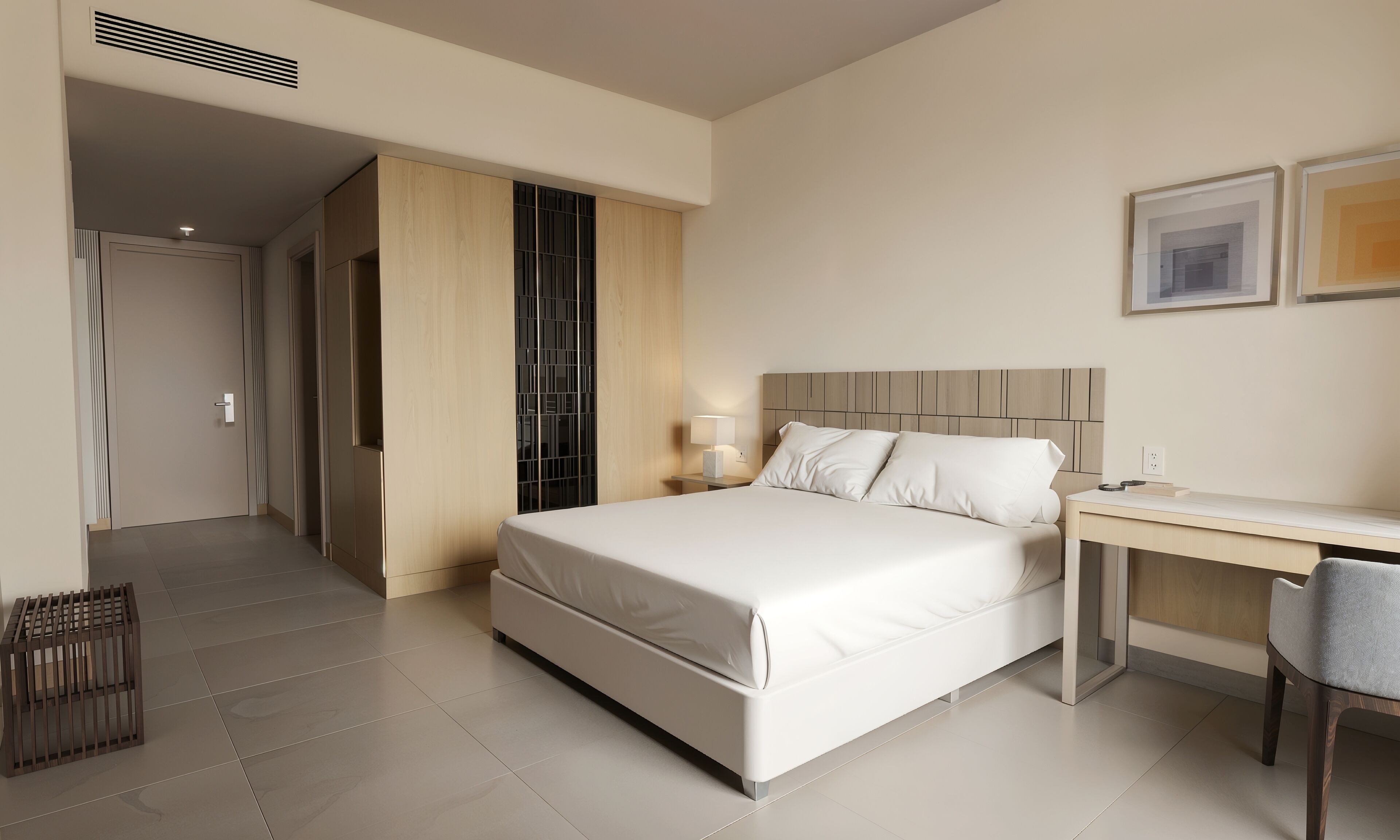 A hotel room with a bed, bedside table, desk, chair, and a door leading to another room.
