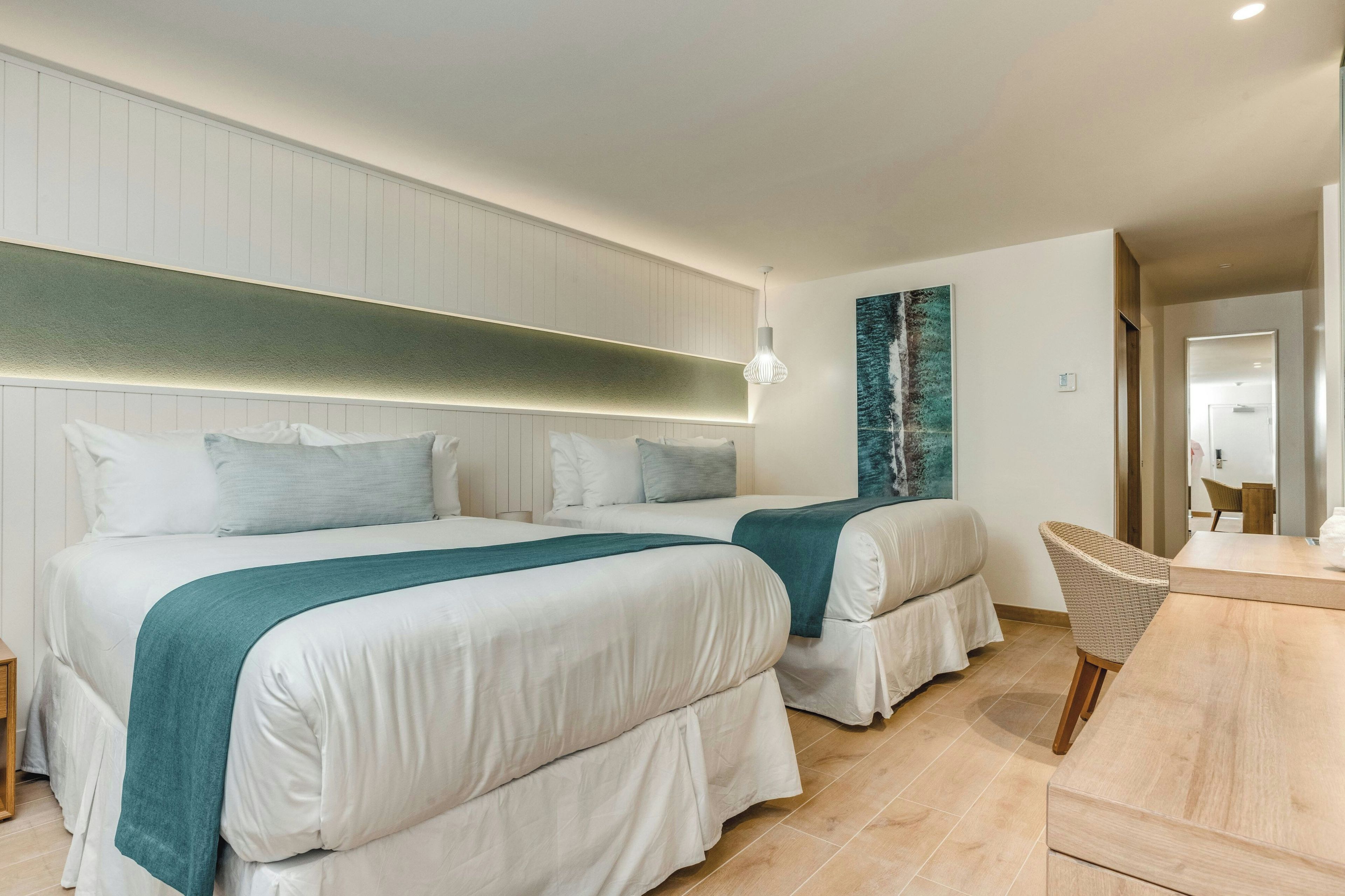A hotel room with two beds, a wooden desk, a chair, and a large painting on the wall.