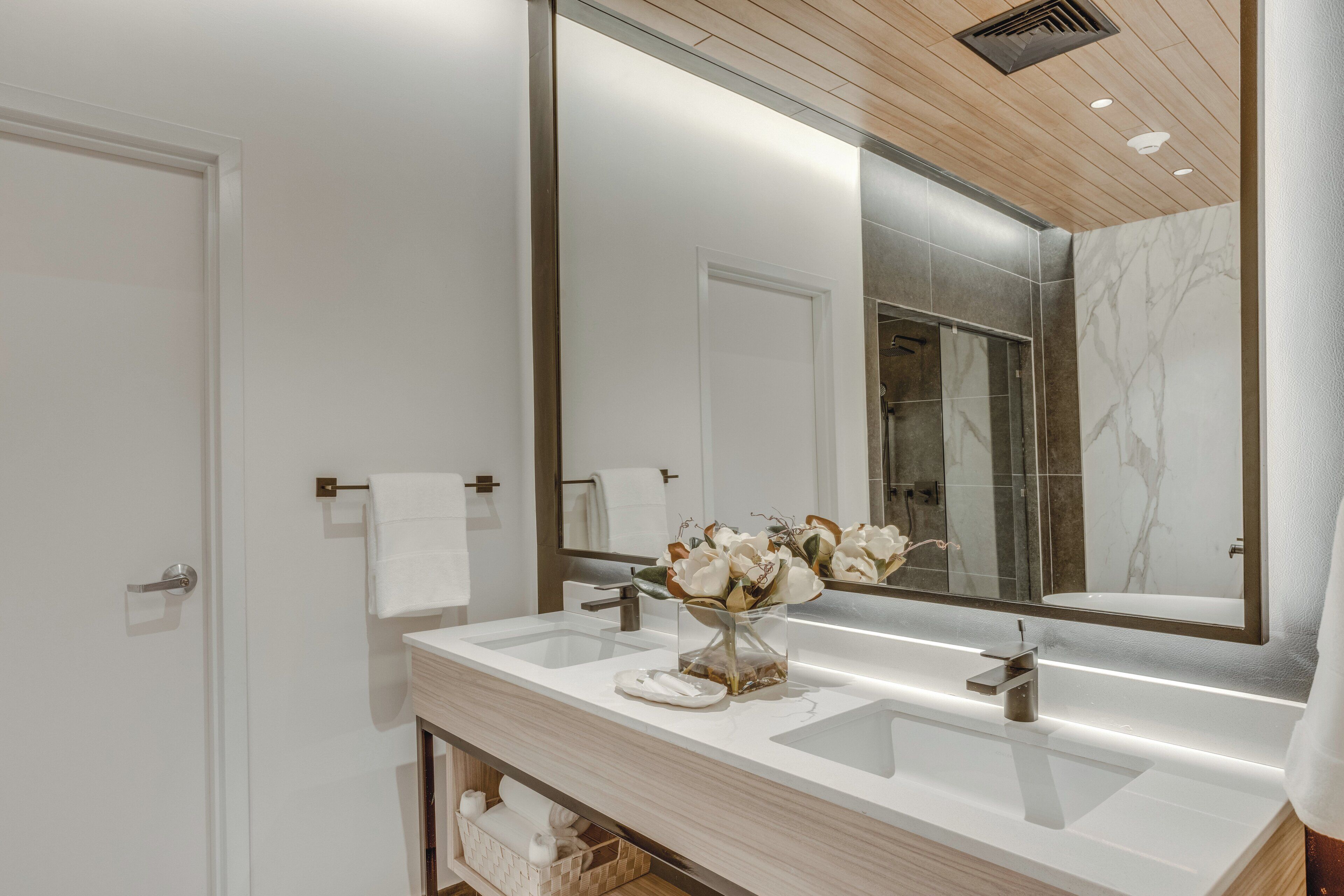A modern bathroom with a large mirror, two sinks, and a vase of flowers.