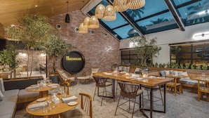 A restaurant with a brick wall, wooden furniture, and hanging lights.
