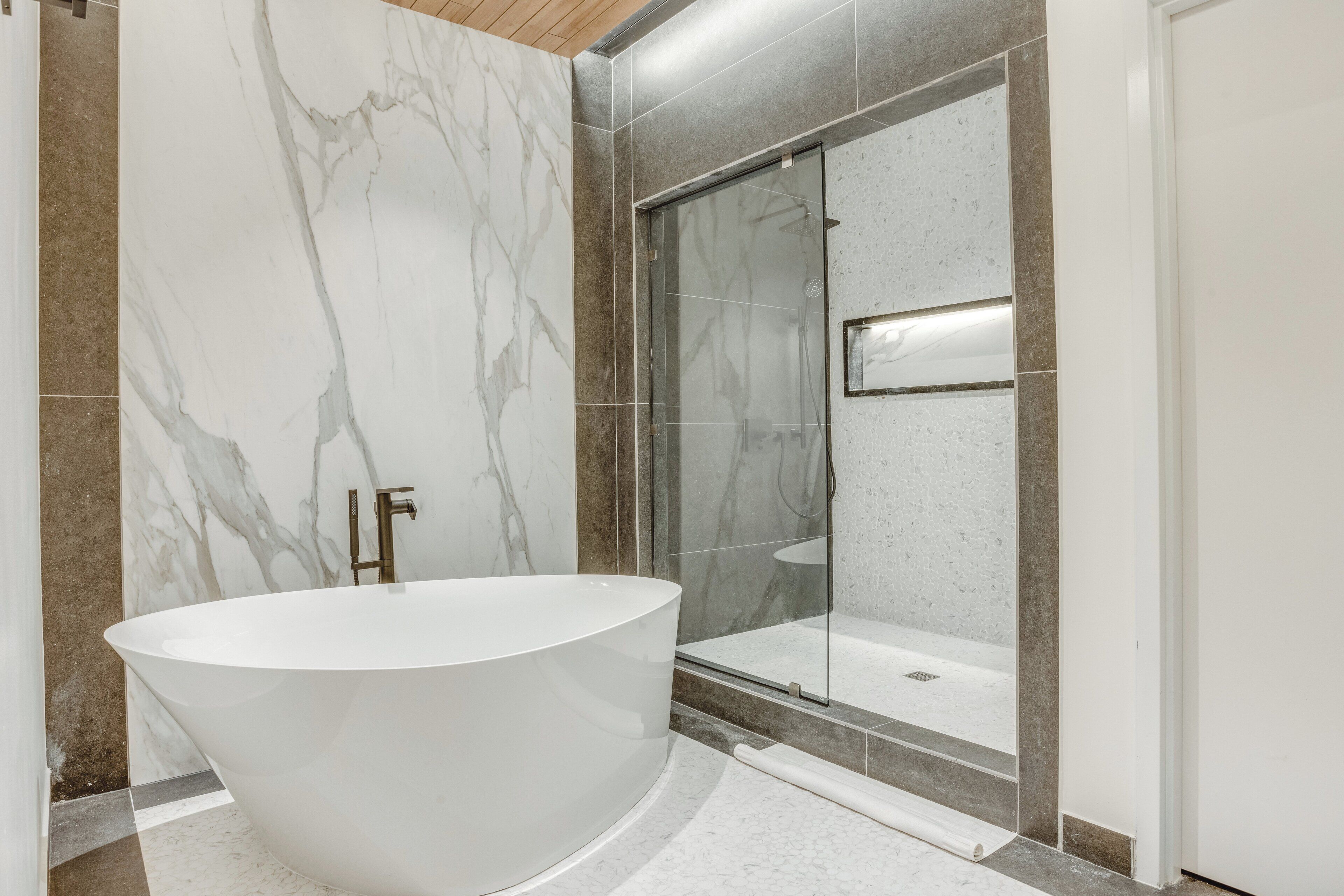 Une salle de bain moderne avec une baignoire sur pieds, une douche en verre et des murs en marbre.